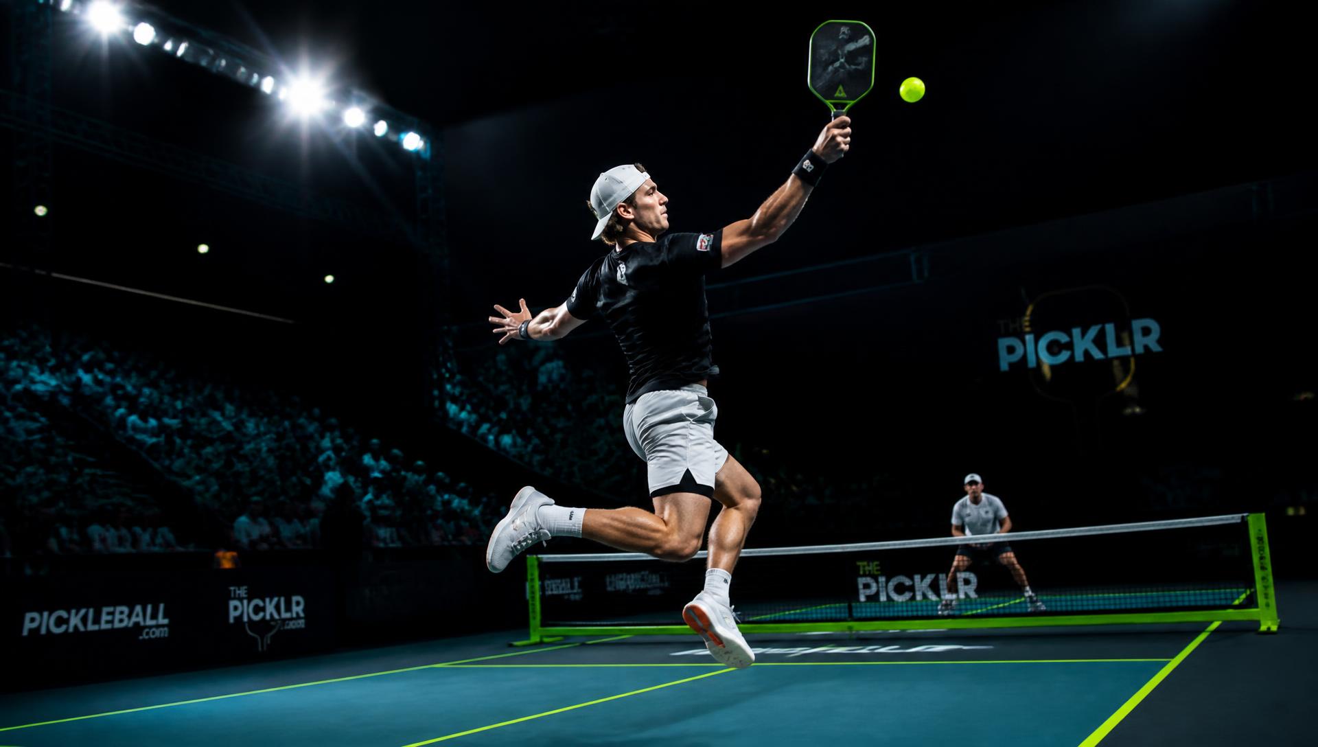 Professional pickleball player striking the ball in a floodlit arena